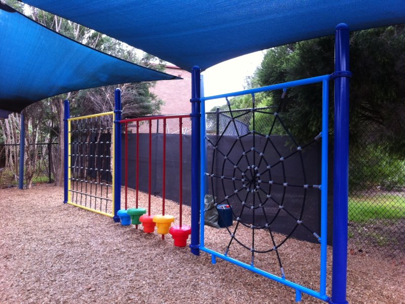 A web-style net panel connects to a square climbing net with built-in step forms, creating a fun transition between elements. Bright blue posts support the structure and match the rest of the playground’s vibrant color scheme. It’s all part of a custom-designed climbing circuit at an elementary school in Brisbane, Australia.