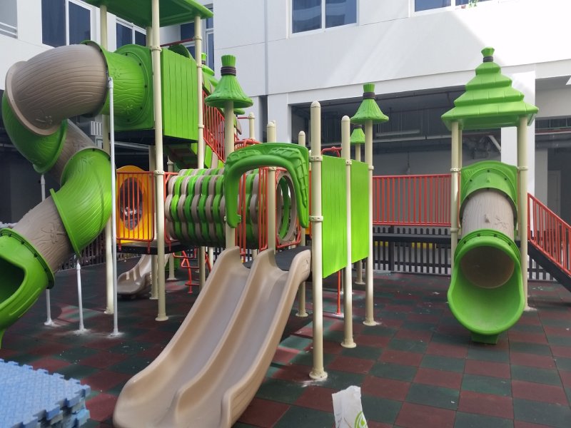 Nature-inspired outdoor playground with green tunnels, beige double slides, and tree alike canopy roofs in a school courtyard setting in Dubai.