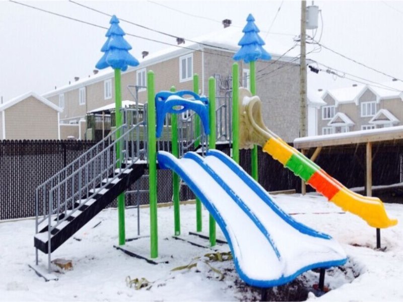 Colorful evergreen tree themed outdoor playground with blue double slide and rainbow wave slide in a residential townhouse complex.