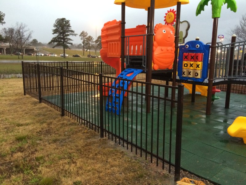 This vibrant playset was designed for a shopping centre playground in the Midwest United States. Featuring a nature-inspired tree theme, it includes a single orange curved slide, a yellow double straight slide, a blue arch climber, and several orange play panels. A cognitive number board adds an educational element for younger children. The structure is topped with green tree-themed accents, along with one yellow and one blue roof. Suitable for children ages 2 to 12, this photo highlights the blue arch climber.
