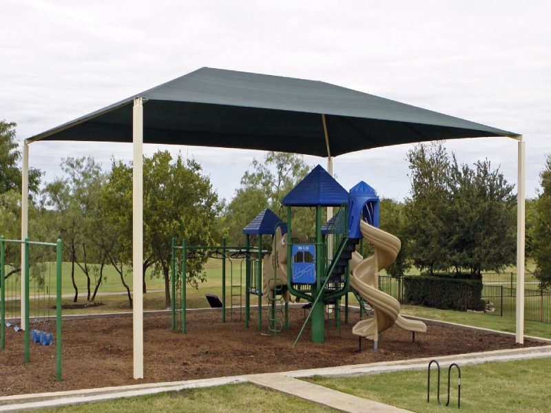 This mid-sized outdoor playset was custom-designed for a public park in Southern Texas. It features a KidsVenture Classic Series play structure tailored for children ages 5 to 12. The play system includes an 8-foot-high beige spiral slide and a matching 6-foot-high straight slide, offering varied levels of excitement for different age groups. Access to the decks is provided by a two-rung ladder and a ring climber, encouraging physical activity and coordination. Connected to the main structure is a swirling overhead climber, similar to a monkey bar, adding an extra layer of challenge and fun. Bold blue traditional plastic roofs top the structure, giving it a vibrant yet sturdy appearance. Nearby, two swings complete the play area, offering a well-rounded recreational experience for children of all abilities.