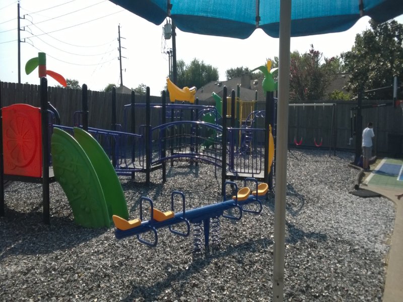 This custom-designed project was created for an elementary school outdoor playground. It features a variety of play elements suitable for children ages 2 to 12. A 5-foot-high standalone play structure with a bright yellow railing and a vibrant green spiral slide adds excitement for older kids. A classic monkey bar invites children ages 4 and up to test their courage and upper-body strength. Multiple net climbers challenge children of all ages to develop balance and coordination. The lower deck, equipped with two small purple parallel slides, creates a welcoming space for younger children to play together and build social skills. The inclusive design also ensures children with disabilities can enjoy outdoor play in a safe and engaging environment. Nearby, a swing offers younger children the thrill of motion while helping them bond with caregivers. This photo highlights the seesaw.