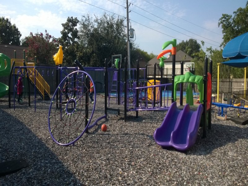 This custom-designed project was created for an elementary school outdoor playground. It features a variety of play elements suitable for children ages 2 to 12. A 5-foot-high standalone play structure with a bright yellow railing and a vibrant green spiral slide adds excitement for older kids. A classic monkey bar invites children ages 4 and up to test their courage and upper-body strength. Multiple net climbers challenge children of all ages to develop balance and coordination. The lower deck, equipped with two small purple parallel slides, creates a welcoming space for younger children to play together and build social skills. The inclusive design also ensures children with disabilities can enjoy outdoor play in a safe and engaging environment. Nearby, a swing offers younger children the thrill of motion while helping them bond with caregivers. This photo highlights the eye-catching purple slides and the circular net climber in action.
