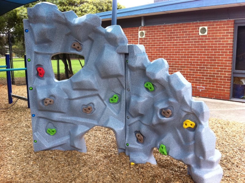 This climbing wall features a textured gray surface that mimics real rock, paired with colorful handholds for a fun, engaging challenge. An internal support structure ensures strength and stability. It’s part of a custom-designed climbing circuit at an elementary school in Brisbane, Australia.