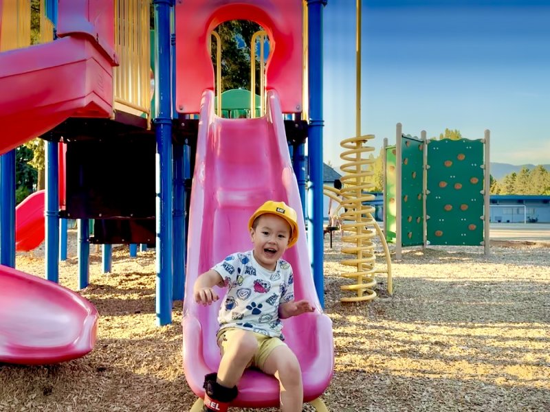 KidsVenture commercial outdoor playground creates memorable experience for kids. A happy little boy sliding down a red slide with big smile on this face.