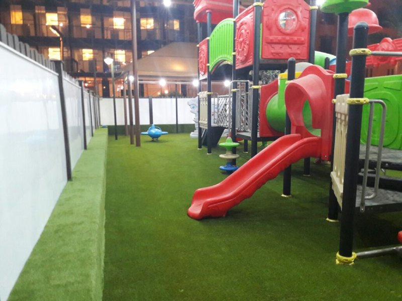Colorful outdoor playground playset at a five-star hotel in Riyadh, featuring slides, climbers, steeping forms, net climbing, and artificial turf under a well-lit canopy. This photo captures the colorful disc climber and open straight slide.